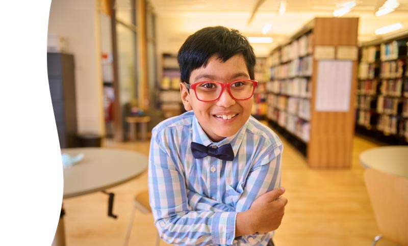 A child with glasses in front of a library setting
